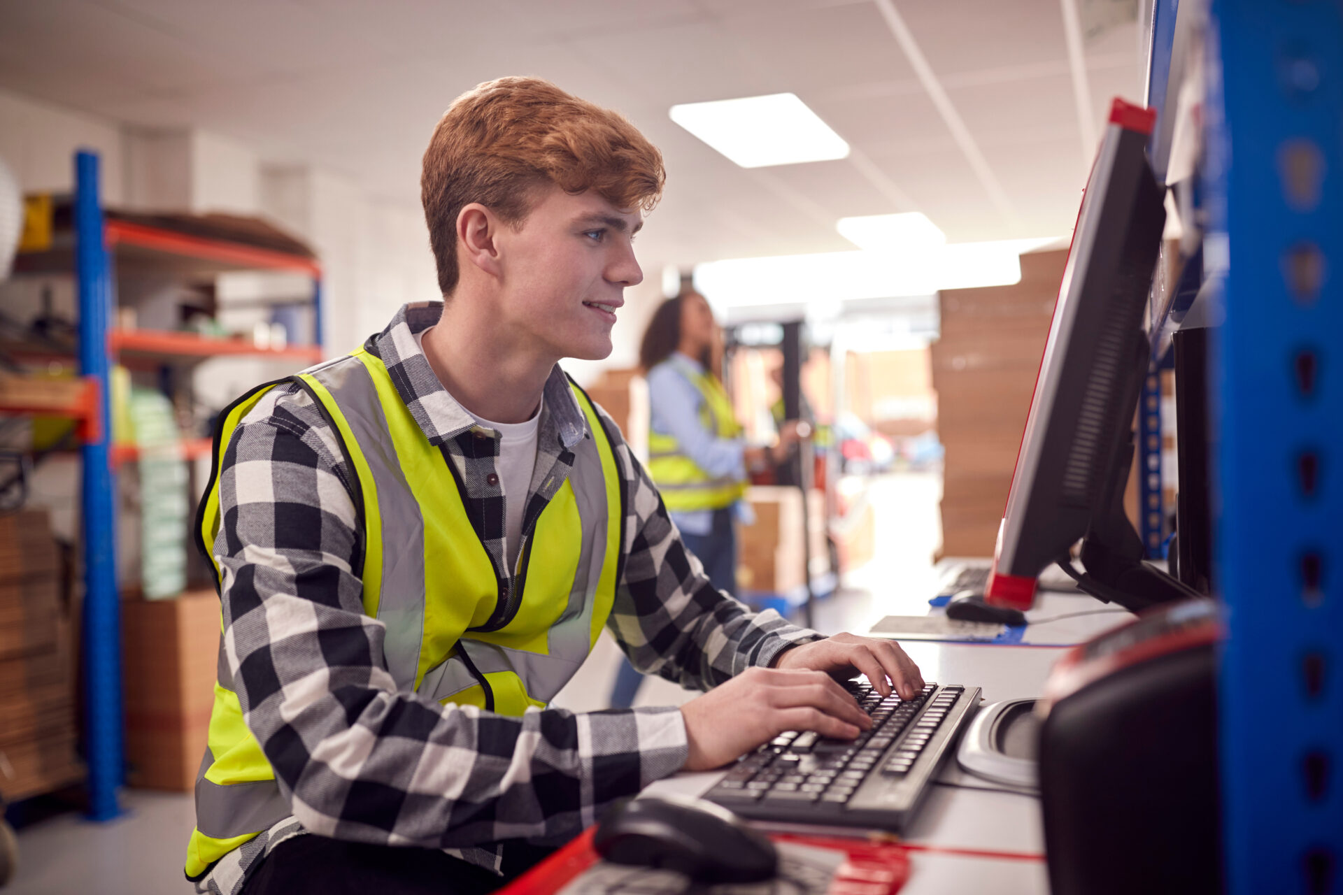 Male intern working in busy modern warehouse on computer termina